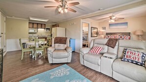 A living room with a ceiling fan, a dining area with wooden chairs, and a kitchen in the background. - Rockport Bayfront Studio w/ Patio: 'casa Familia' (Rockport)