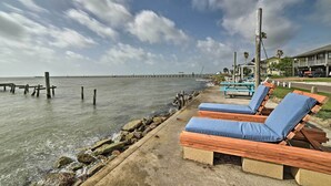 A beachside area with wooden lounge chairs and a concrete walkway along the water. - Rockport Bayfront Studio w/ Patio: 'casa Familia' (Rockport)