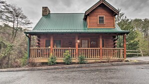 A log cabin with a green metal roof, a wooden porch, and a chimney.