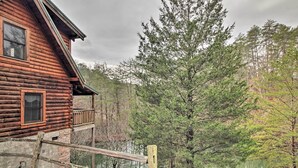 A log cabin with a balcony overlooking a forested area and a body of water.