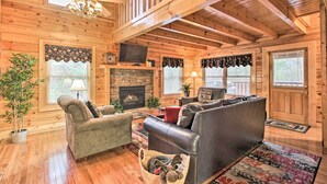 A log cabin interior with a fireplace, leather sofas, and a television.