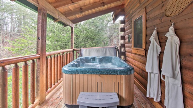 A wooden cabin with a hot tub on a deck, surrounded by trees.