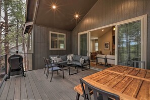 Une terrasse extérieure avec une table et des chaises en bois, un barbecue et un canapé avec des coussins.