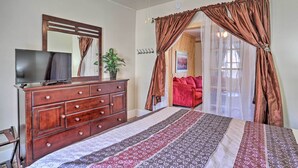 Een slaapkamer met een bed, een kapstok, een televisie, een spiegel, een plant en een deur naar een andere kamer.
