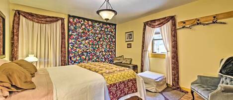 Quarto com cama, cadeira, mesa de cabeceira, parede com padrão colorido e luminária no teto.