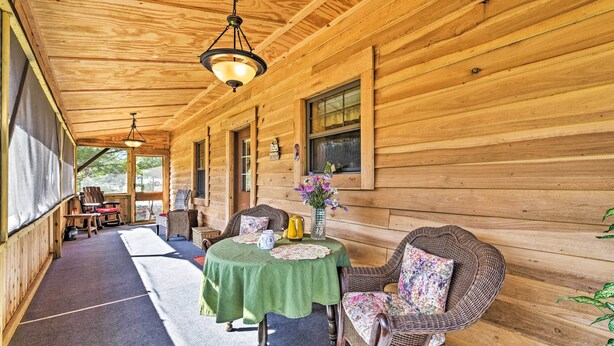 A wooden cabin with a covered porch, furnished with wicker chairs and a table set with a pitcher, vase, and teapot. - 'honey House Cabin' - A Quiet Countryside Retreat! (Nappanee)