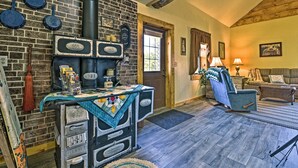 A rustic interior with a brick wall, a vintage stove, a wooden ceiling, and a cozy seating area with a sofa and armchair. - 'honey House Cabin' - A Quiet Countryside Retreat! (Nappanee)