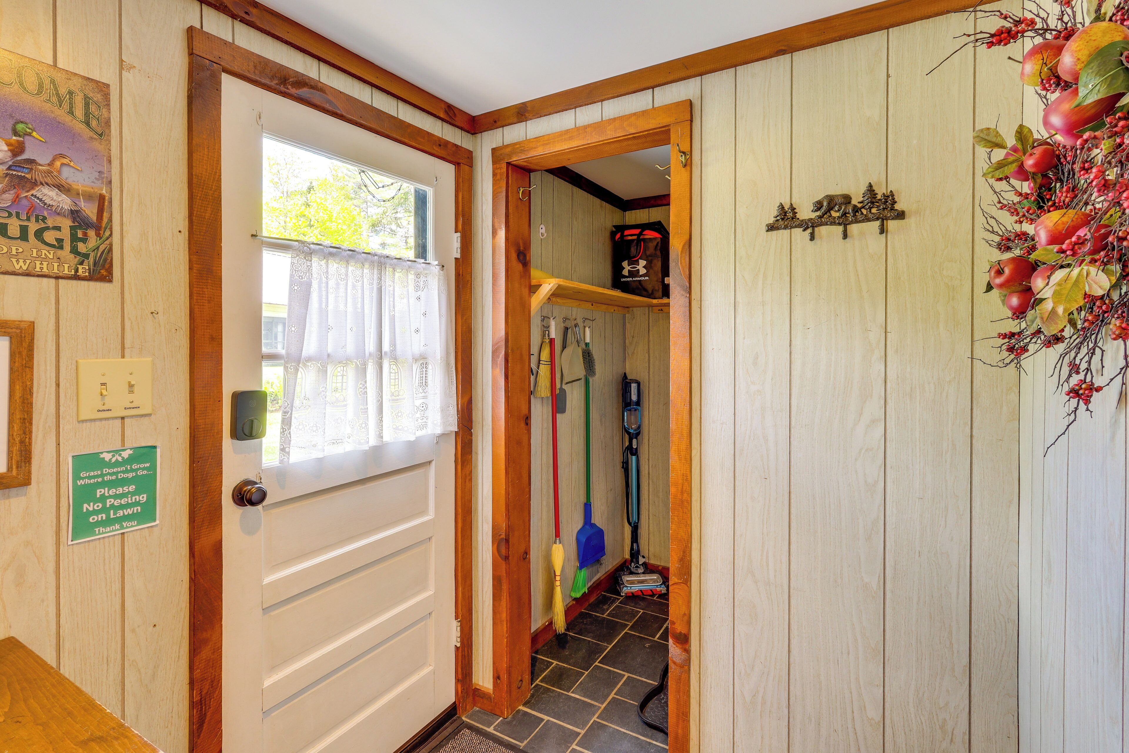 Una puerta de madera con un letrero que solicita no orinar en el césped, una ventana con cortina y un pasillo con utensilios de limpieza.