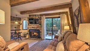 A cozy living room with a stone fireplace, wooden beams, a comfortable sofa, and a television.