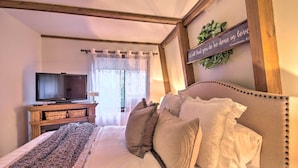 A bedroom with a bed, a television on a stand, a window with sheer curtains, and a motivational quote on the wall.