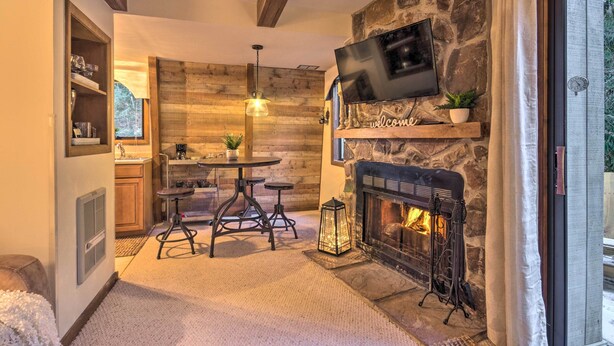 A cozy living area with a stone fireplace, a flat-screen TV mounted above it, and a dining table with stools.