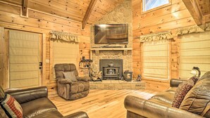 Ein gemütliches Blockhaus-Interieur mit Kamin aus Stein, Ledersofas und einem flachbildfernseher, der über dem Kamin angebracht ist.