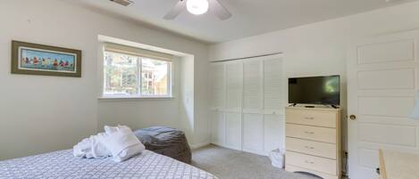 Un dormitorio con cama, ventilador de techo, ventana, televisor, armario y cómoda.