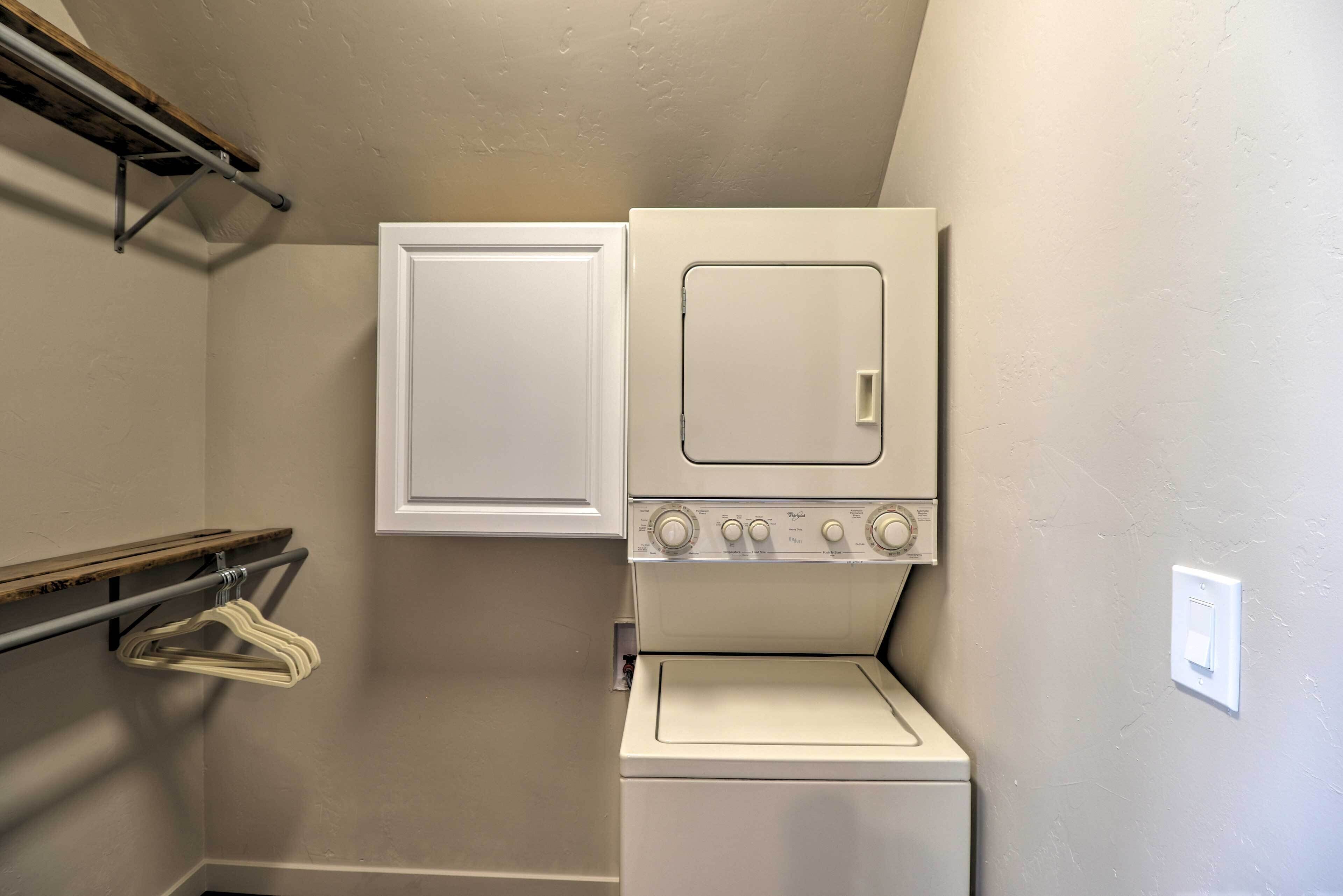 Une buanderie équipée d’un lave-linge et d’un sèche-linge, d’une étagère en métal avec des cintres et d’une porte blanche.