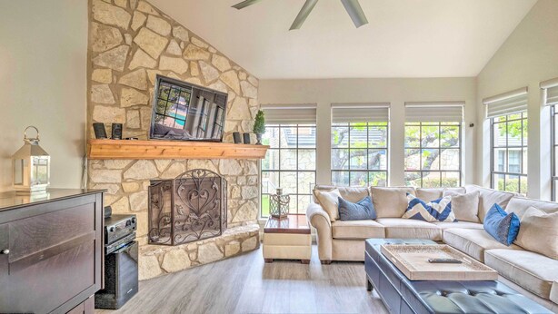 A living room with a stone fireplace, a ceiling fan, and a large window with blinds. - Horseshoe Bay Townhome w/ Patio & Outdoor Pool! (Horseshoe Bay)