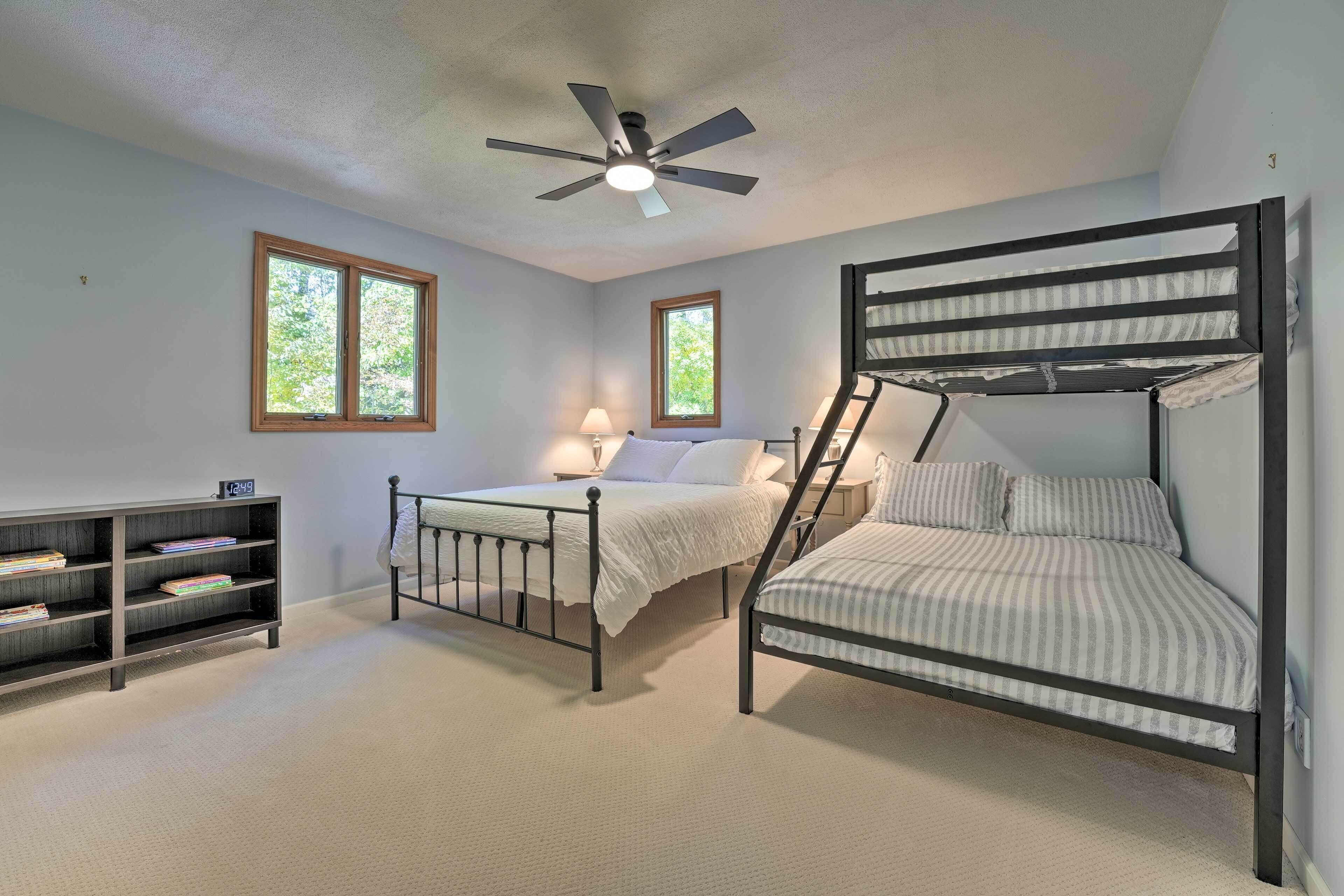 A bedroom with a bunk bed, a desk with a chair, a bookshelf, two windows, and a ceiling fan.