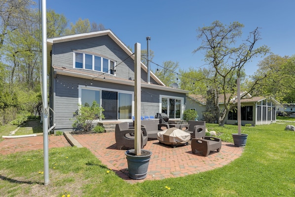A two-story house with a brick patio, outdoor furniture, and a covered grill area. - Spacious Delton Home w/ Fire Pit + Lake Views (Delton)