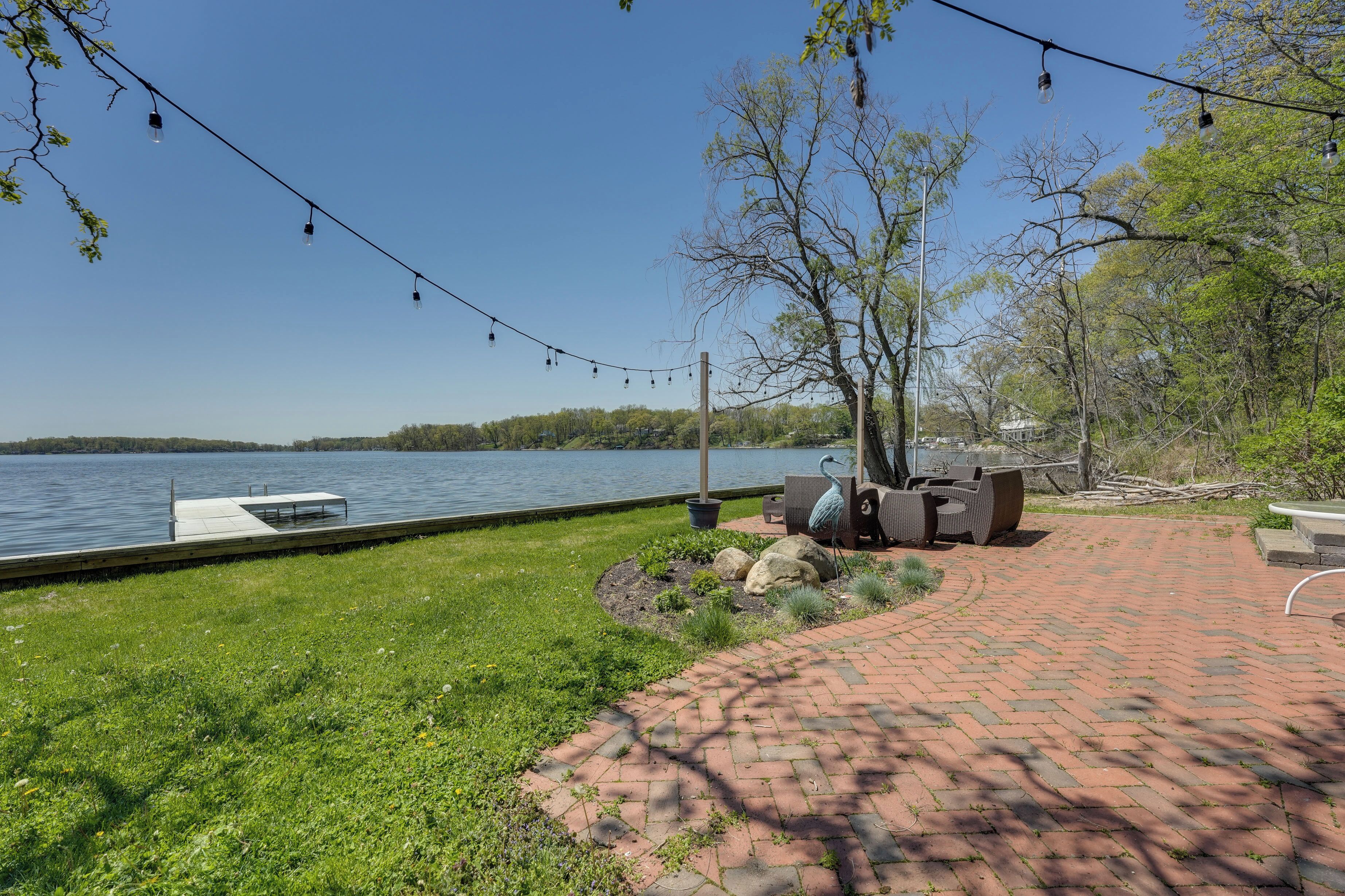 A lakeside patio with a dock, outdoor seating, and string lights.