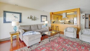 A living room with a sofa, armchairs, a coffee table, and a kitchen area with wooden cabinets and a countertop. - Lincoln City Oceanfront Condo, Near Lincoln Beach! (Gleneden Beach)