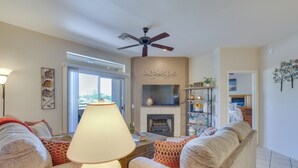 Una sala de estar con chimenea, ventilador de techo y sofá con cojines estampados.