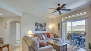 Sala de estar con sofá, mesa de centro y ventilador de techo. Hay una puerta corrediza de vidrio que da a un patio al aire libre con mesa y sillas.
