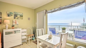 Varanda com vista para o oceano, uma mesa branca com cadeiras, uma pequena planta e um objeto decorativo na mesa.