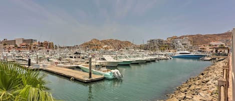A marina with boats docked, rocky shoreline, and buildings in the background.