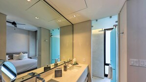 A modern hotel bathroom with a large mirror, a sink, and a toilet. There is a bed visible in the adjacent room. - Upscale Cabo Home w/ Jacuzzi, Above Puerto Paraiso (Cabo San Lucas)
