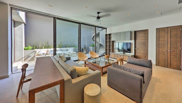 A modern living room with a sofa, coffee table, and chairs, a TV, and wooden cabinets. - Upscale Cabo Home w/ Jacuzzi, Above Puerto Paraiso (Cabo San Lucas)