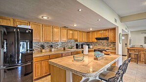 A modern kitchen with wooden cabinets, a stainless steel refrigerator, a large island with bar stools, and a stone backsplash. - Waterfront Home in Parker w/ Mtn Views & Dock! (Parker)