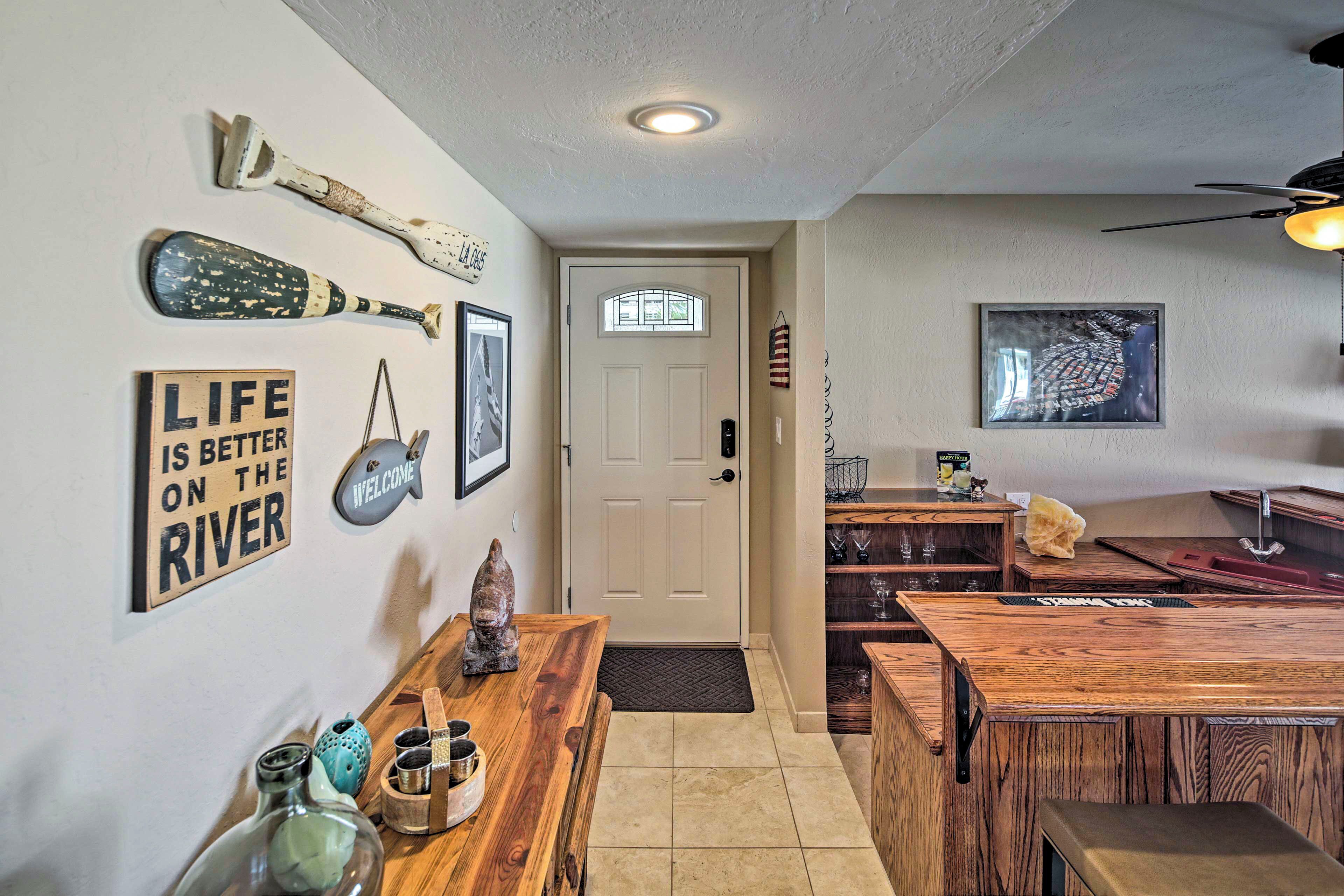 A home interior with a wooden dining table, a bench, a door with a window, and various wall decorations including a baseball bat and a welcome sign.