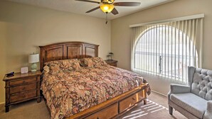 A bedroom with a large bed, a ceiling fan, a window with blinds, a nightstand, and a chair. - Waterfront Home in Parker w/ Mtn Views & Dock! (Parker)