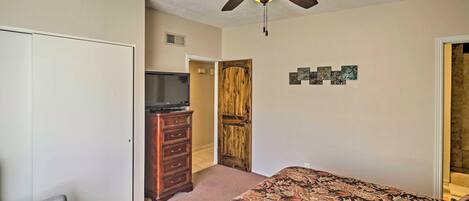 A bedroom with a bed, a dresser, a television, a ceiling fan, and a door.