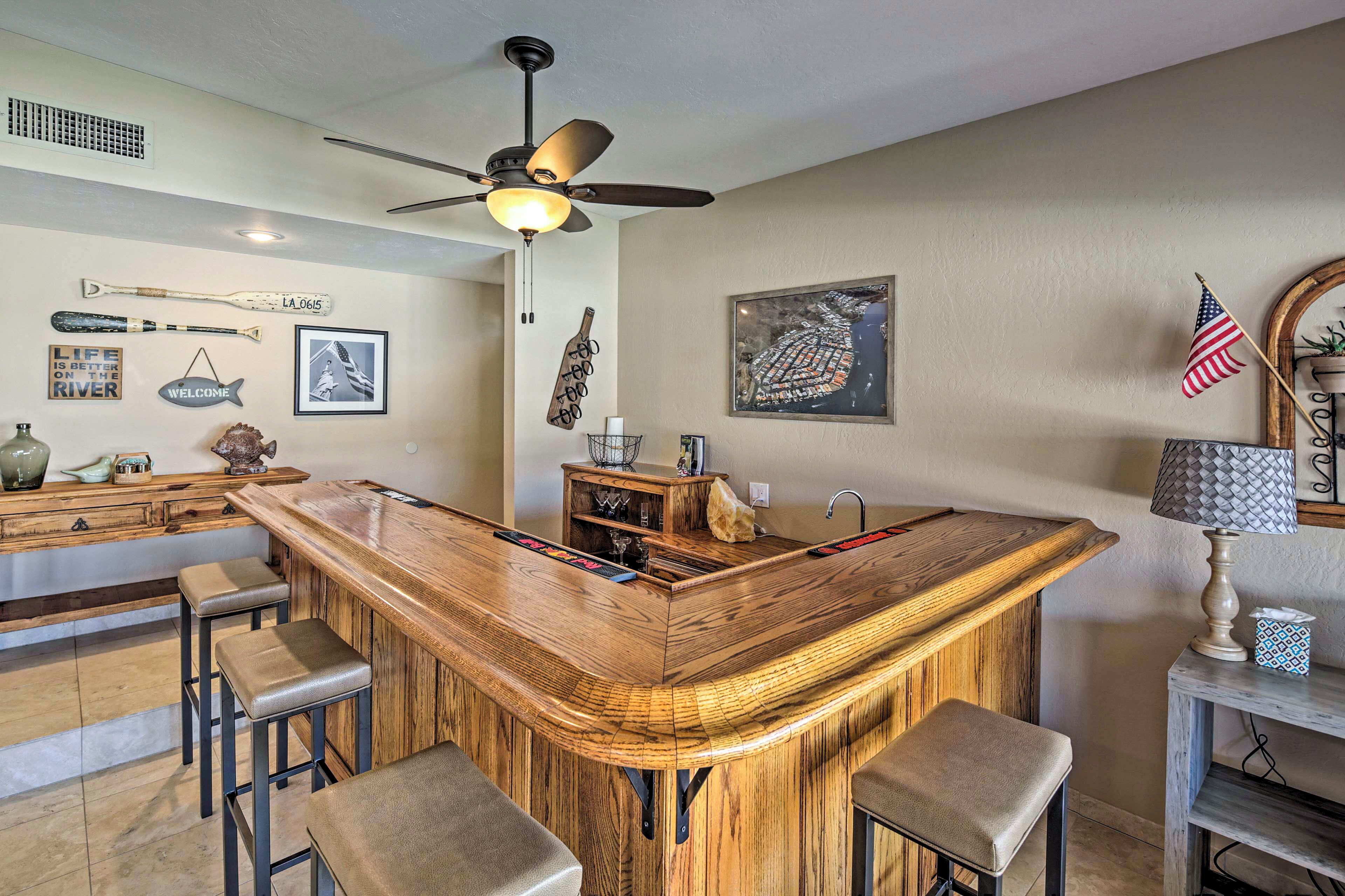 A kitchen with a wooden bar, bar stools, a ceiling fan, and various wall decorations including a fish sign and a welcome sign.