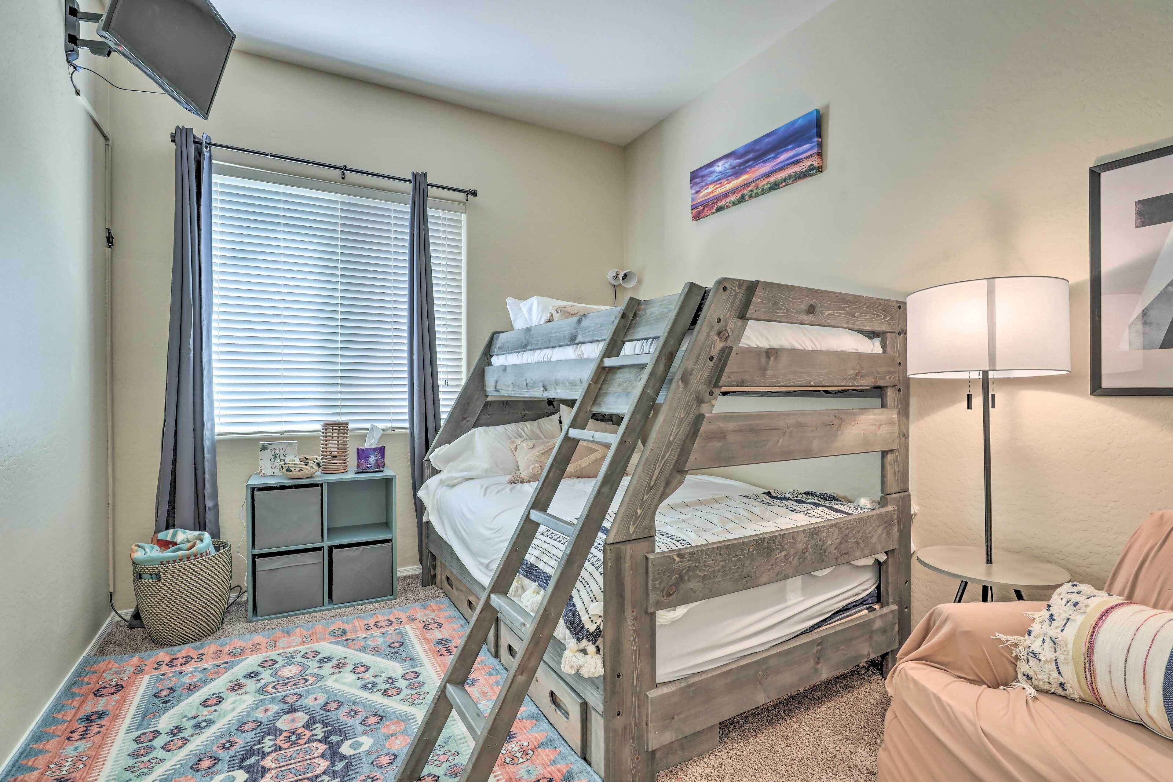 A bunk bed room with a ladder, a small table, a lamp, and a patterned rug.
