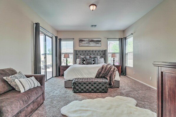 A bedroom with a large bed, a sofa, a tufted ottoman, and a white fur rug. - Near Golf & Spring Training: Goodyear Home w/ Pool (Goodyear)