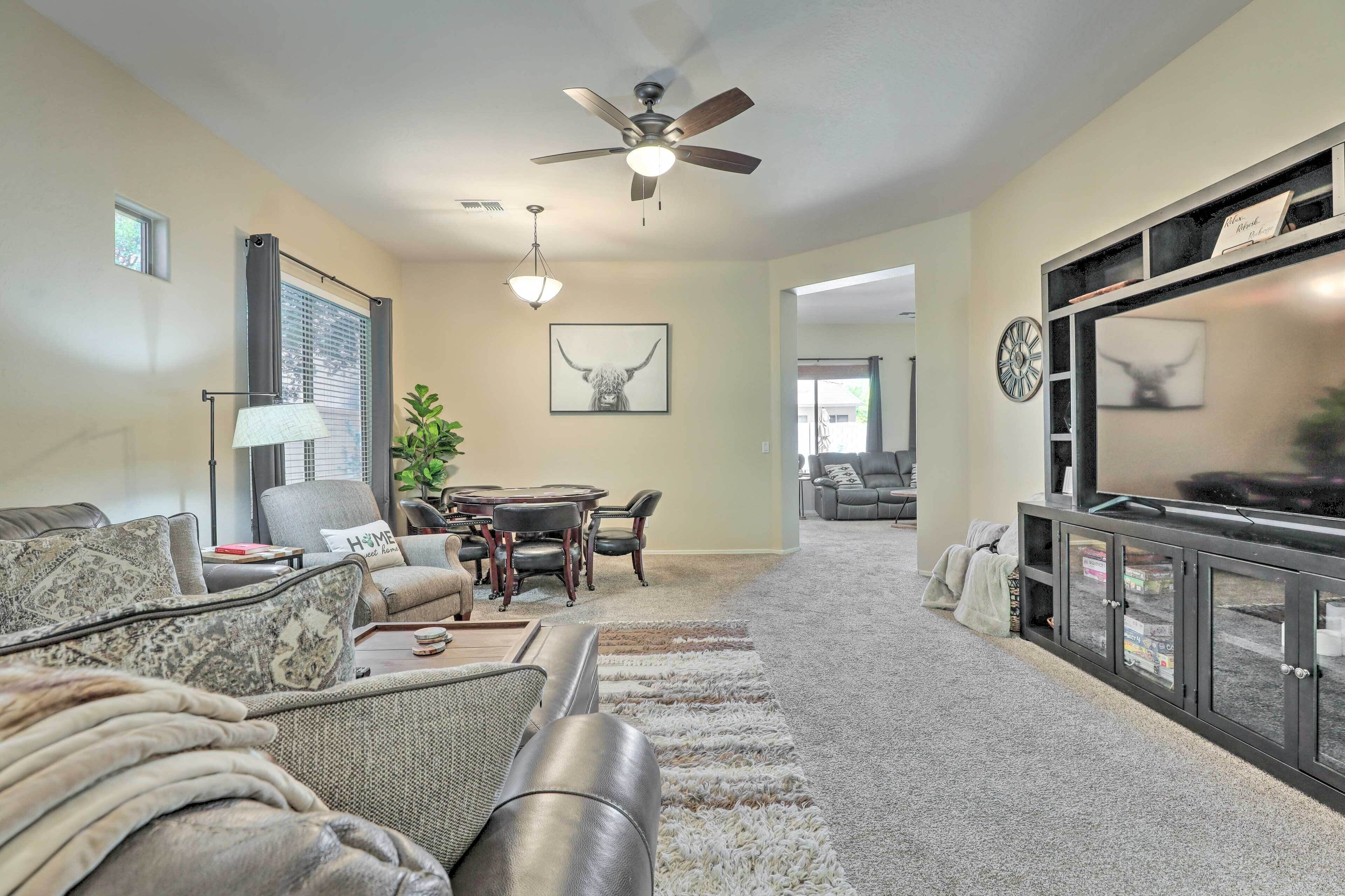 A living room with a sofa, a coffee table, a dining table with chairs, a ceiling fan, and a TV stand with glass doors.
