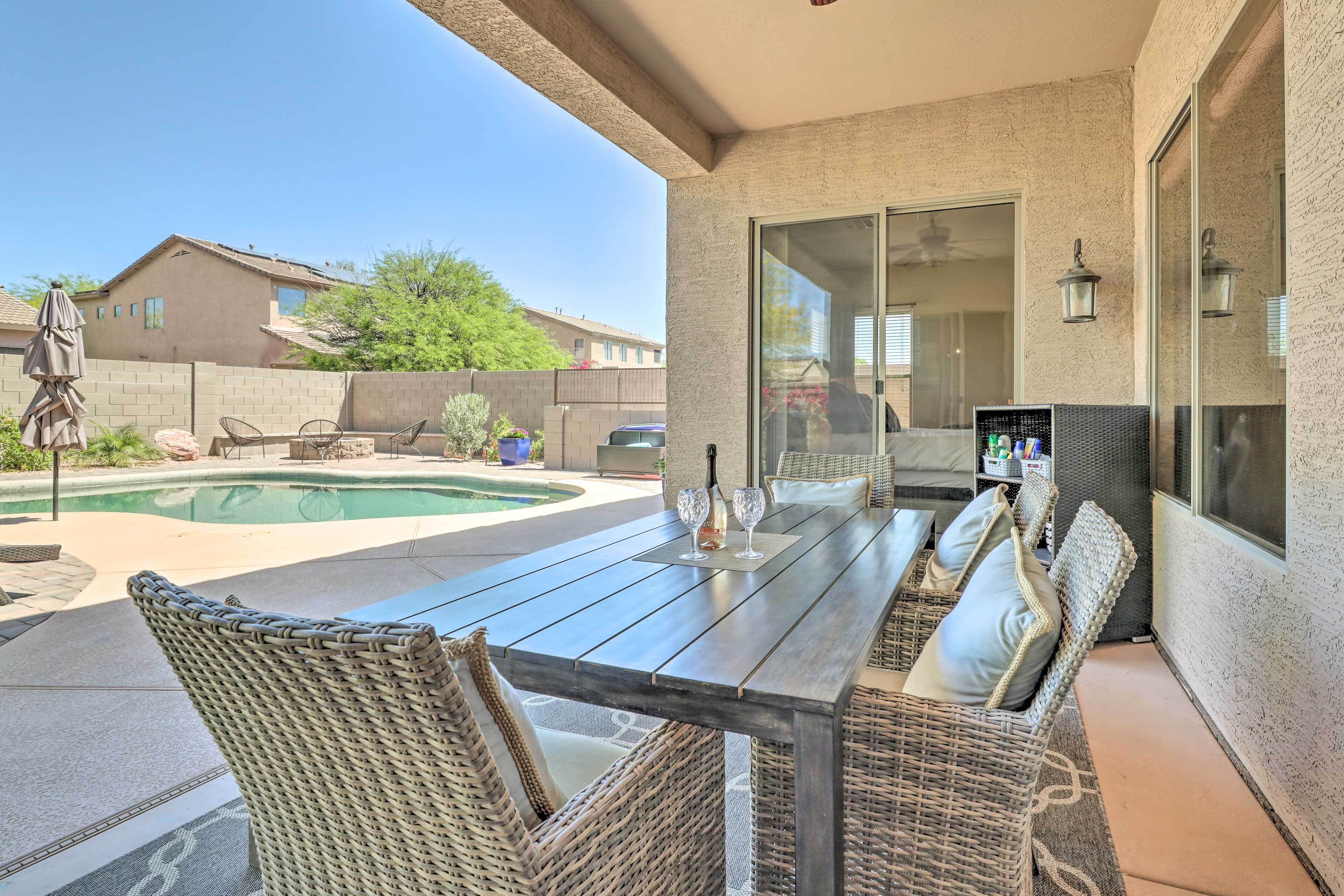 A patio with a pool, wicker furniture, and a glass-enclosed dining area.
