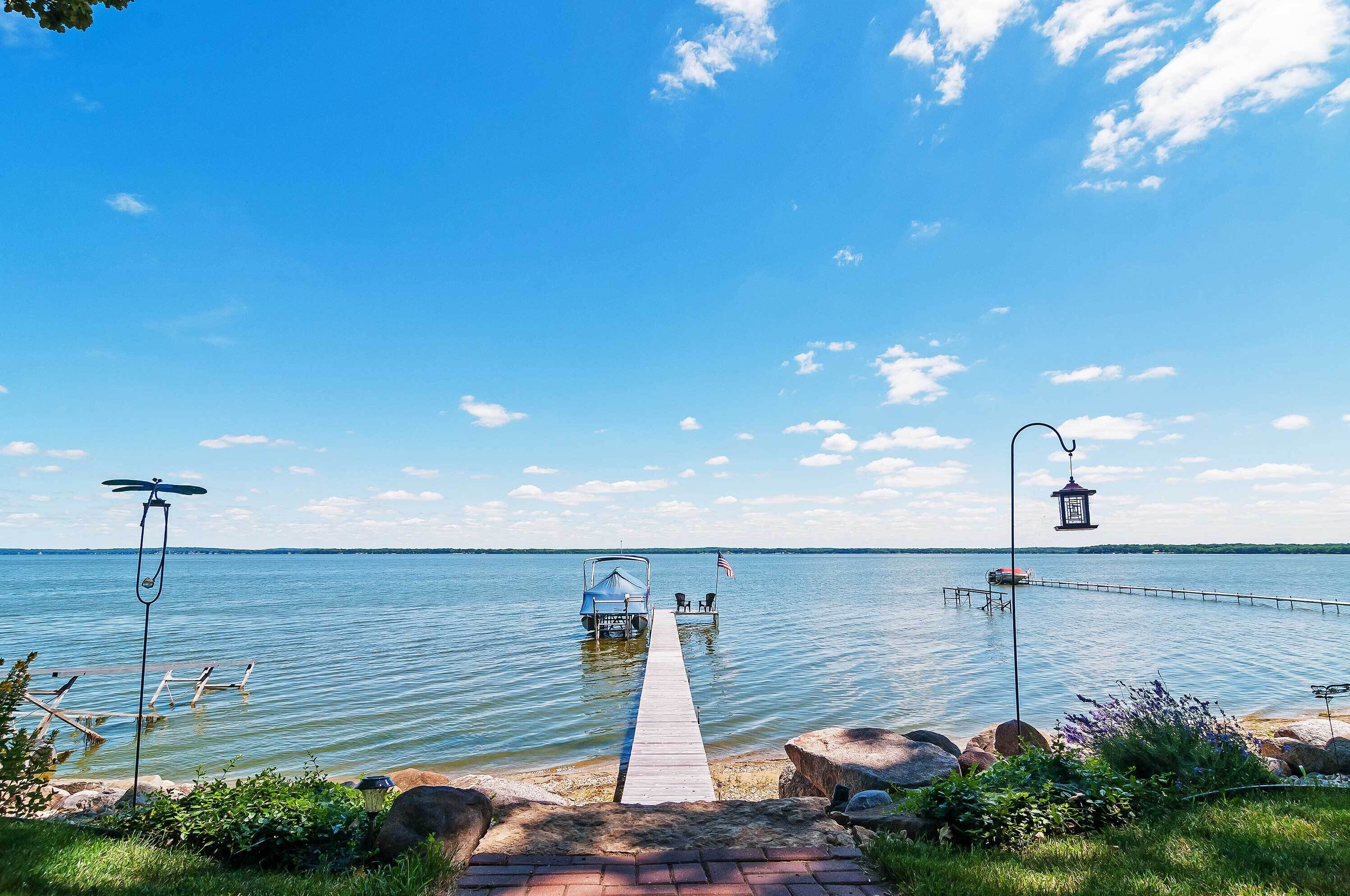 A wooden dock extending into a calm lake with a small boat and a gazebo.