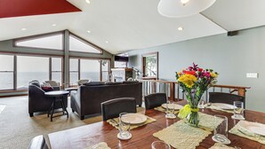 A dining area with a view of the sea, a kitchen in the background, and a large window. - Spacious Edgerton Home w/ Private Beach & Views! (Edgerton)