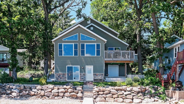 A two-story house with a stone retaining wall, a wooden dock, and a clear view of the water. - Spacious Edgerton Home w/ Private Beach & Views! (Edgerton)