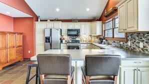 A kitchen with a large island, white cabinets, and a tiled backsplash. - Spacious Edgerton Home w/ Private Beach & Views! (Edgerton)