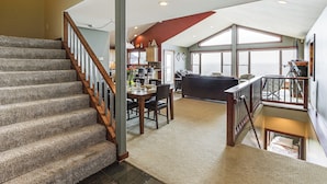 A spacious interior with a staircase leading to a loft area, a dining area, and large windows offering views. - Spacious Edgerton Home w/ Private Beach & Views! (Edgerton)