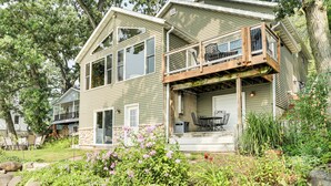 A two-story house with a balcony, a front porch, and a garden with flowers. - Spacious Edgerton Home w/ Private Beach & Views! (Edgerton)