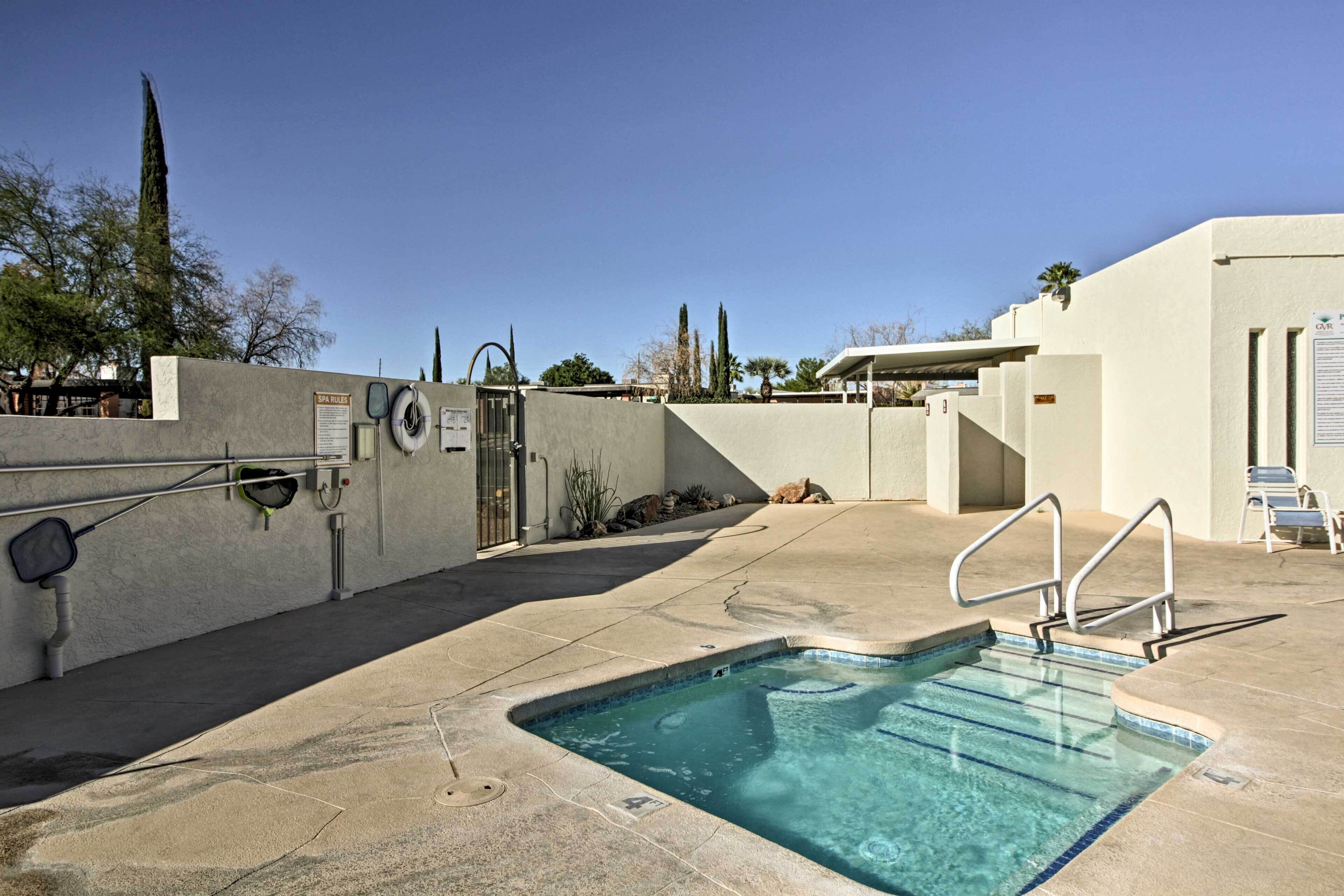 A swimming pool with a clear blue water, surrounded by a concrete deck, and a metal fence.