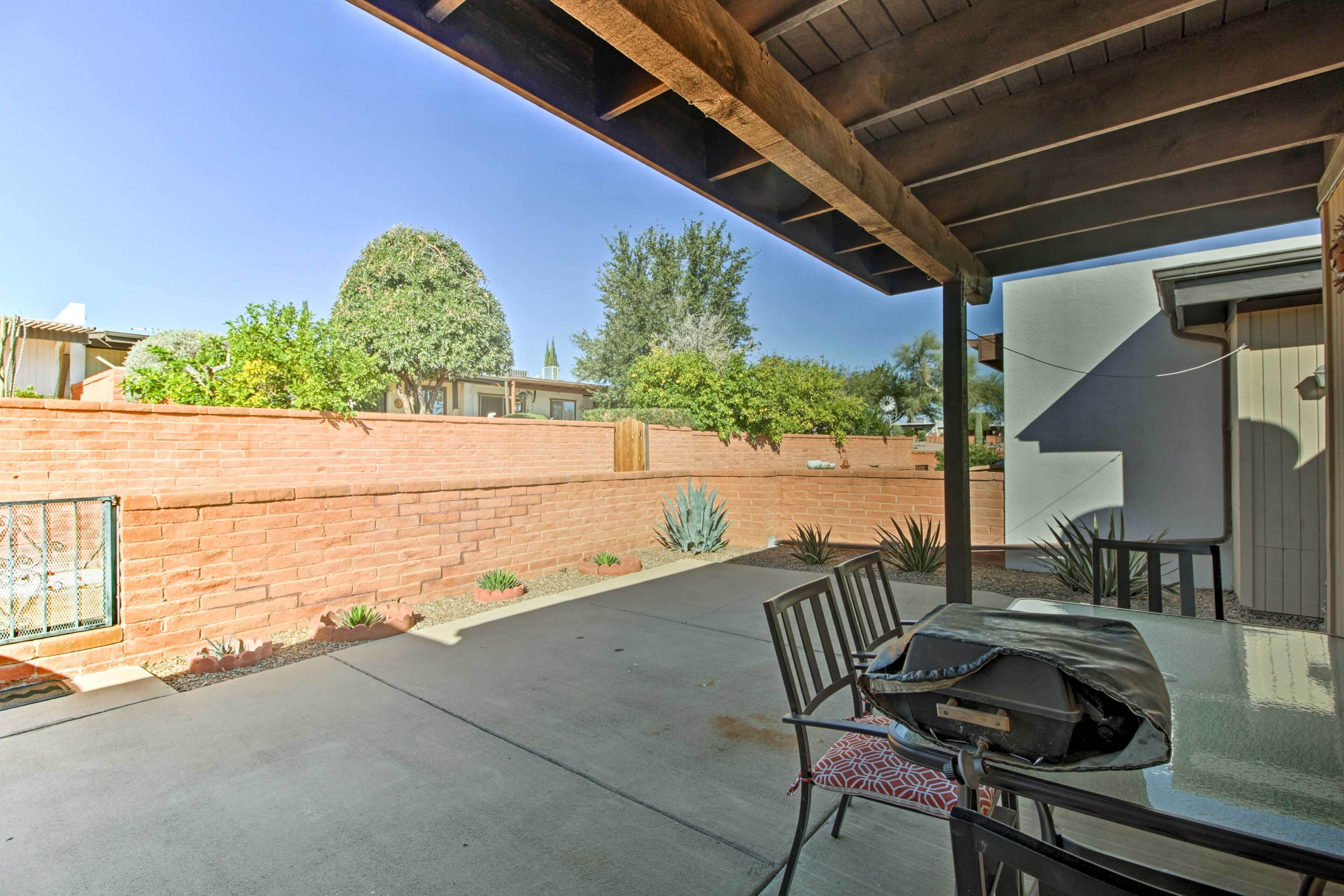 A covered patio with a table and chairs, a brick wall, and a view of the neighborhood.