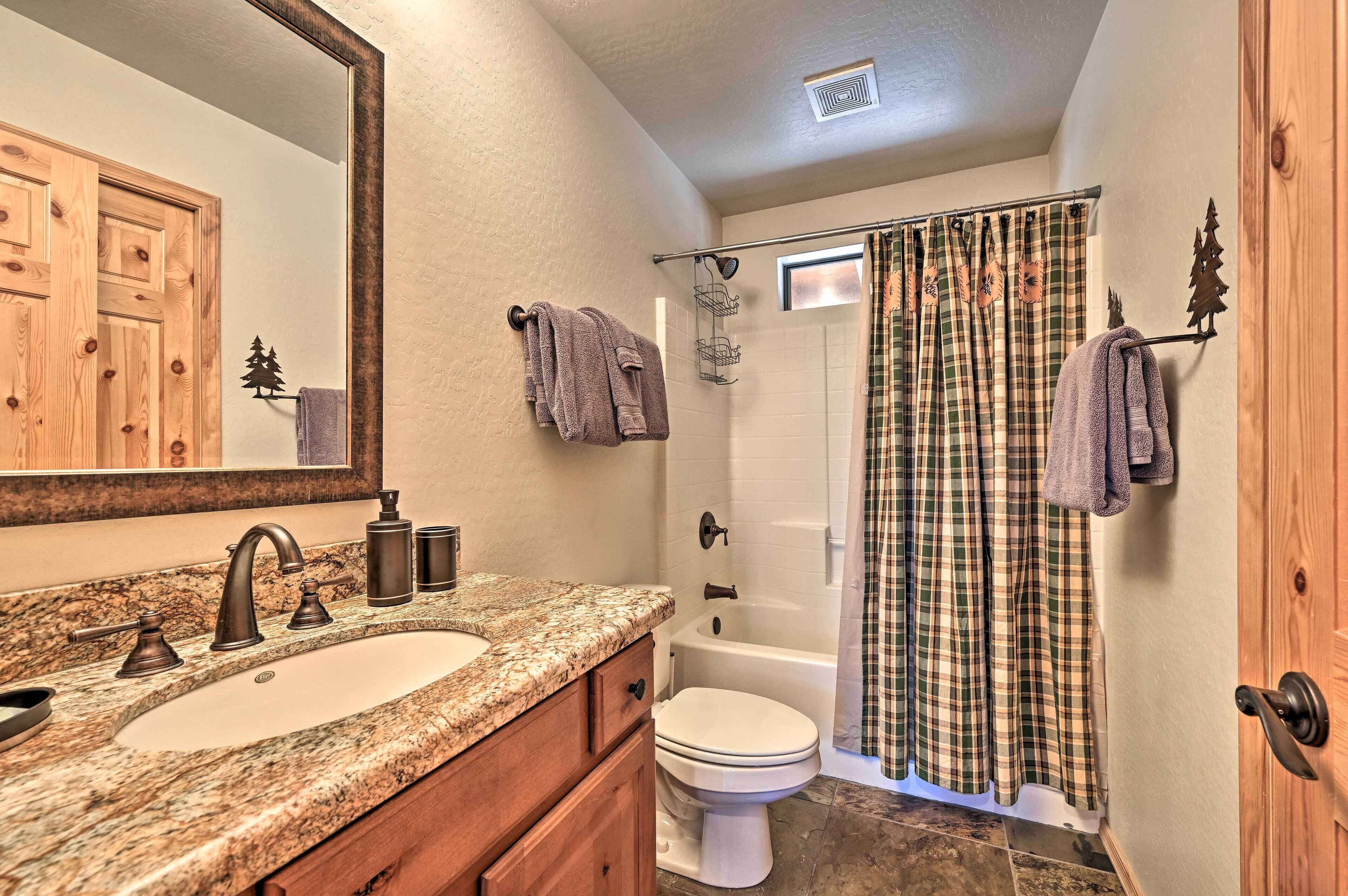 Une salle de bain avec un lavabo sur un plan de travail en granit, des toilettes, une baignoire et un rideau de douche.