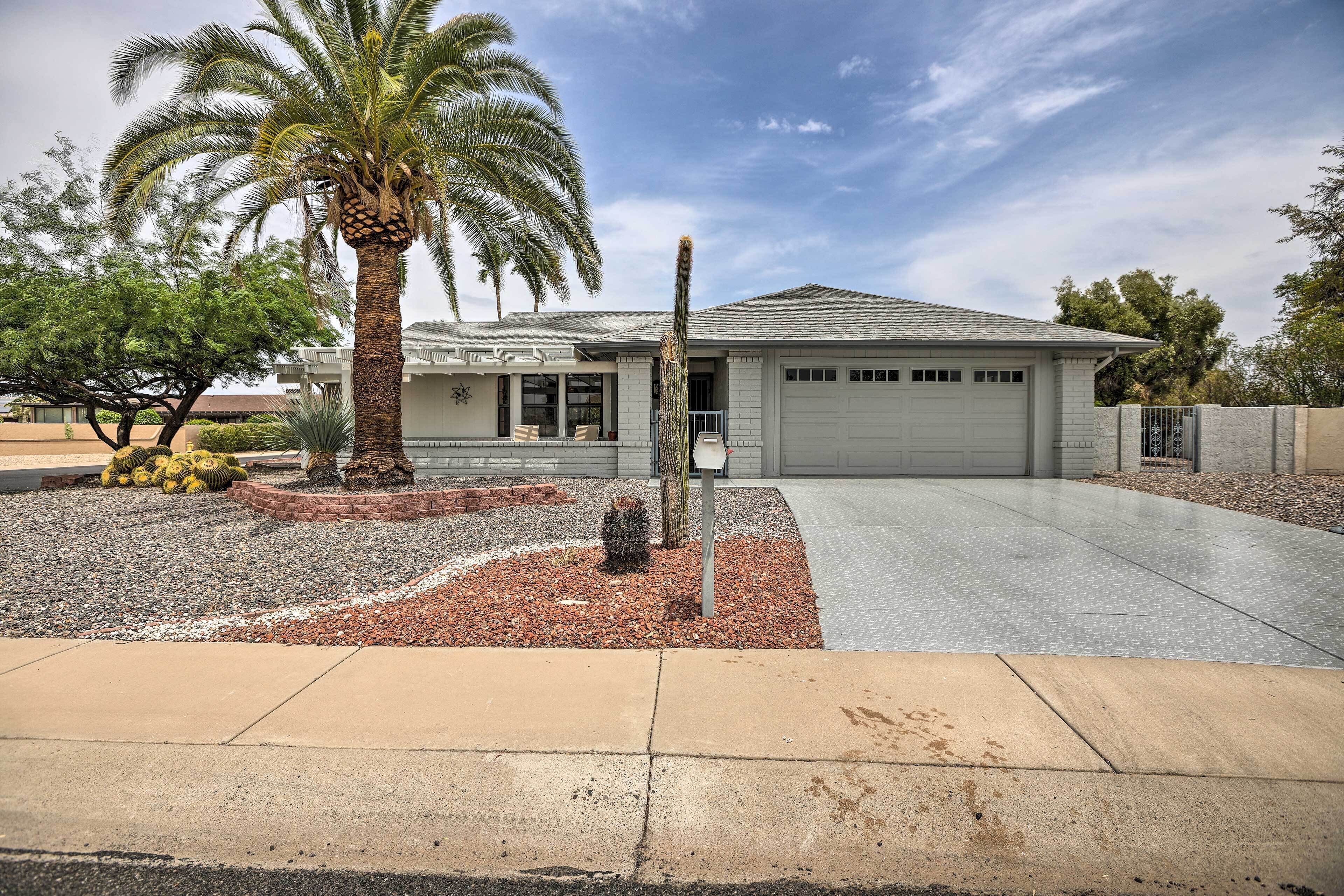 A modern two-story house with a garage, a well-maintained garden with palm trees, and a paved driveway.