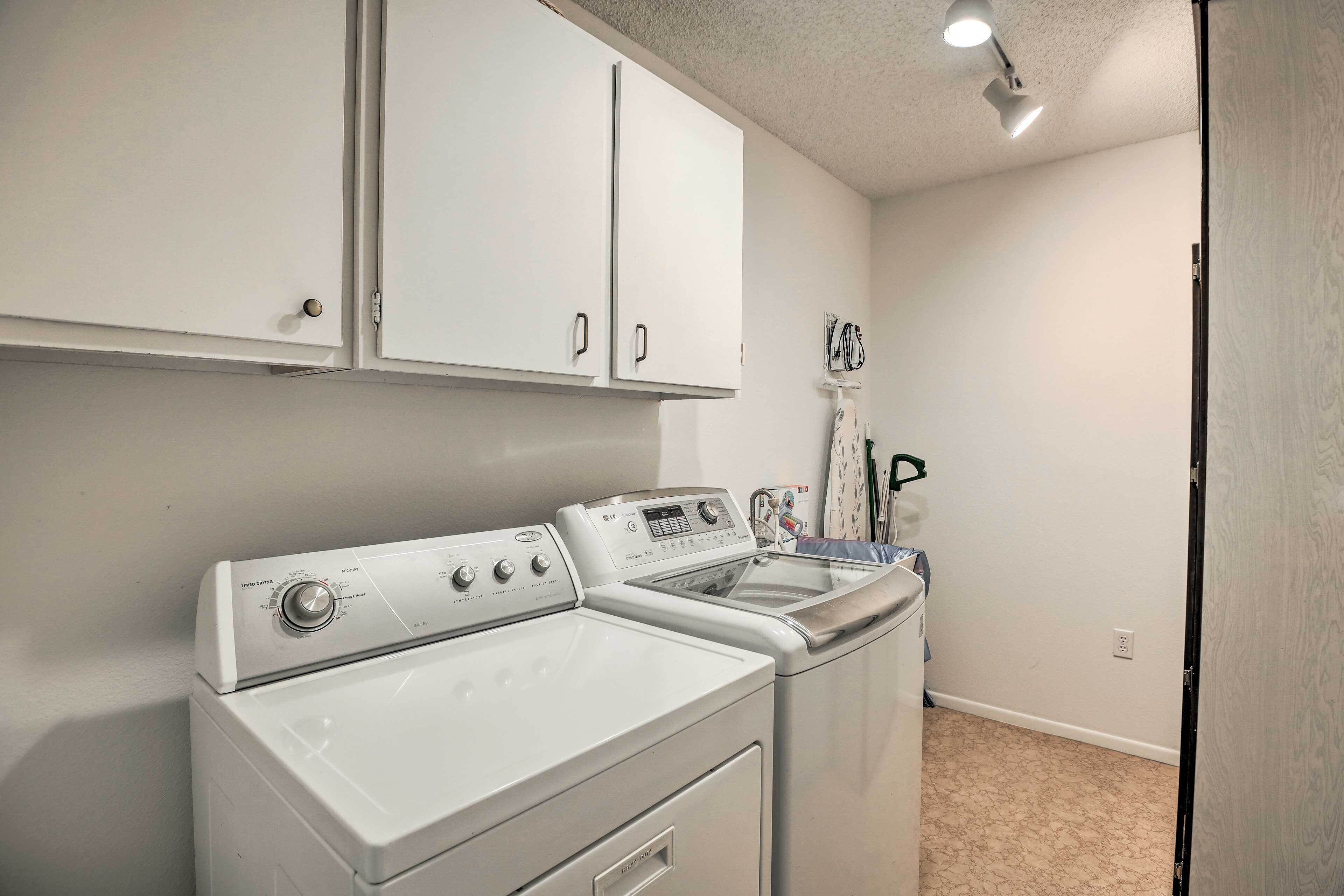 A laundry area with a front-loading washer and dryer, a drying rack, and a ceiling-mounted light fixture.