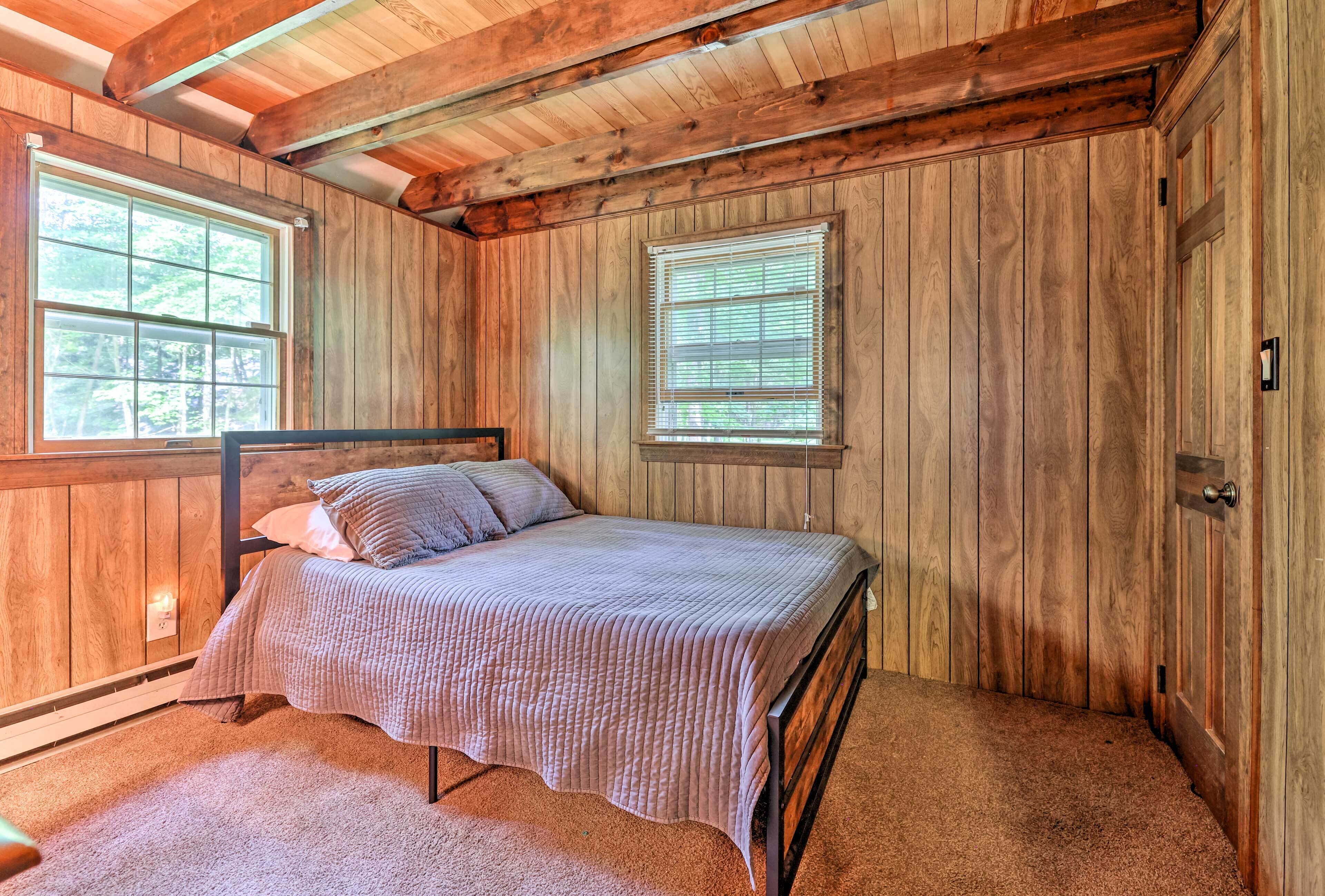 A wooden-paneled bedroom with a bed, two windows, and a door.